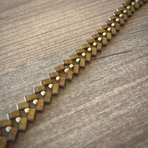May include: A gold and brown metal chain bracelet with a chevron pattern.