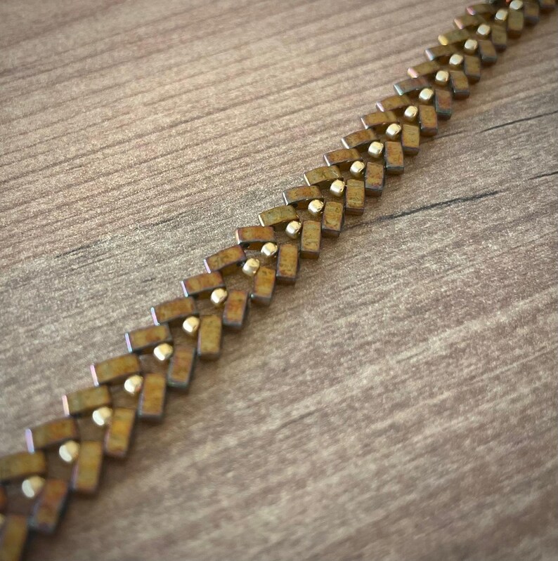May include: A gold and brown metal chain bracelet with a chevron pattern.