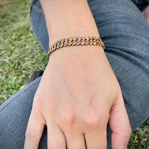 May include: A gold and brown woven bracelet with a geometric pattern.