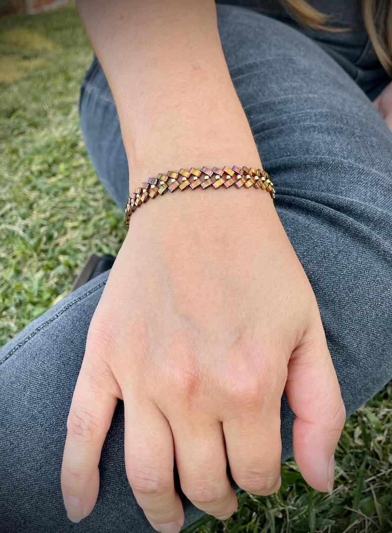 May include: A gold and brown woven bracelet with a geometric pattern.