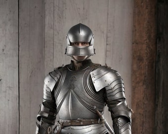 May include: A full suit of medieval armor, crafted from polished steel. The armor includes a helmet, chest plate, shoulder guards, and gauntlets. A sword is held at the side. The image is set against a wooden background.