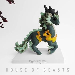 May include: A green and yellow felt Kirin/Qilin mythical creature plush toy. The toy has a long mane and tail, and is standing on a white pedestal. The text "Kirin/Qilin" and "HOUSE OF BEASTS" is printed on the pedestal.