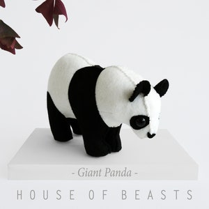 Puede incluir: Un oso de peluche panda blanco y negro, de pie sobre una superficie blanca. El panda está mirando hacia abajo y tiene una nariz negra y ojos negros. El texto "Giant Panda" y "HOUSE OF BEASTS" está impreso debajo del panda.