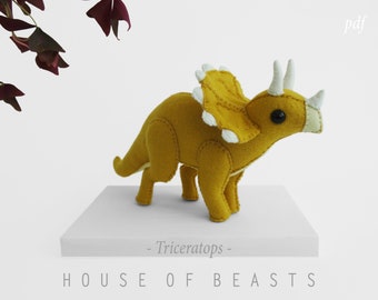 May include: A yellow felt Triceratops plush toy with white felt accents. The toy is standing on a white surface with the text "HOUSE OF BEASTS - Triceratops -" printed below it.