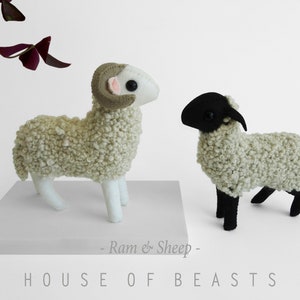 Peut inclure: Patron de jouet en peluche pour un bélier et un mouton, avec le texte "Ram & Sheep" et "HOUSE OF BEASTS" sous les jouets. Le bélier est blanc avec des cornes brunes et un nez rose. Le mouton est blanc avec une tête noire et des pattes noires.