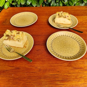 Può includere: Quattro piatti con un dessert con briciole su due dei piatti. I piatti sono di colore marrone chiaro con un motivo decorativo. Il dessert è di colore giallo chiaro con una copertura di briciole marroni.