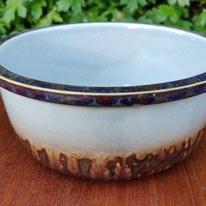 May include: A white ceramic bowl with a brown and blue rim. The bowl has a brown and white glaze with a mottled effect.