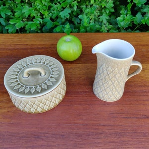 以下が含まれることがあります： 葉の模様が施された薄い緑色のセラミック製のキッチン用品2点セット。セットには、蓋付きのバター入れとクリーマーが含まれています。