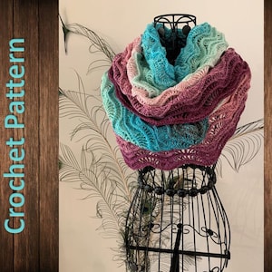 Könnte beinhalten: Ein gehäkeltes Tuch in den Farben Türkis, Rosa und Grün. Das Tuch ist über eine schwarze Schaufensterpuppe gelegt und hat ein welliges, strukturiertes Muster.