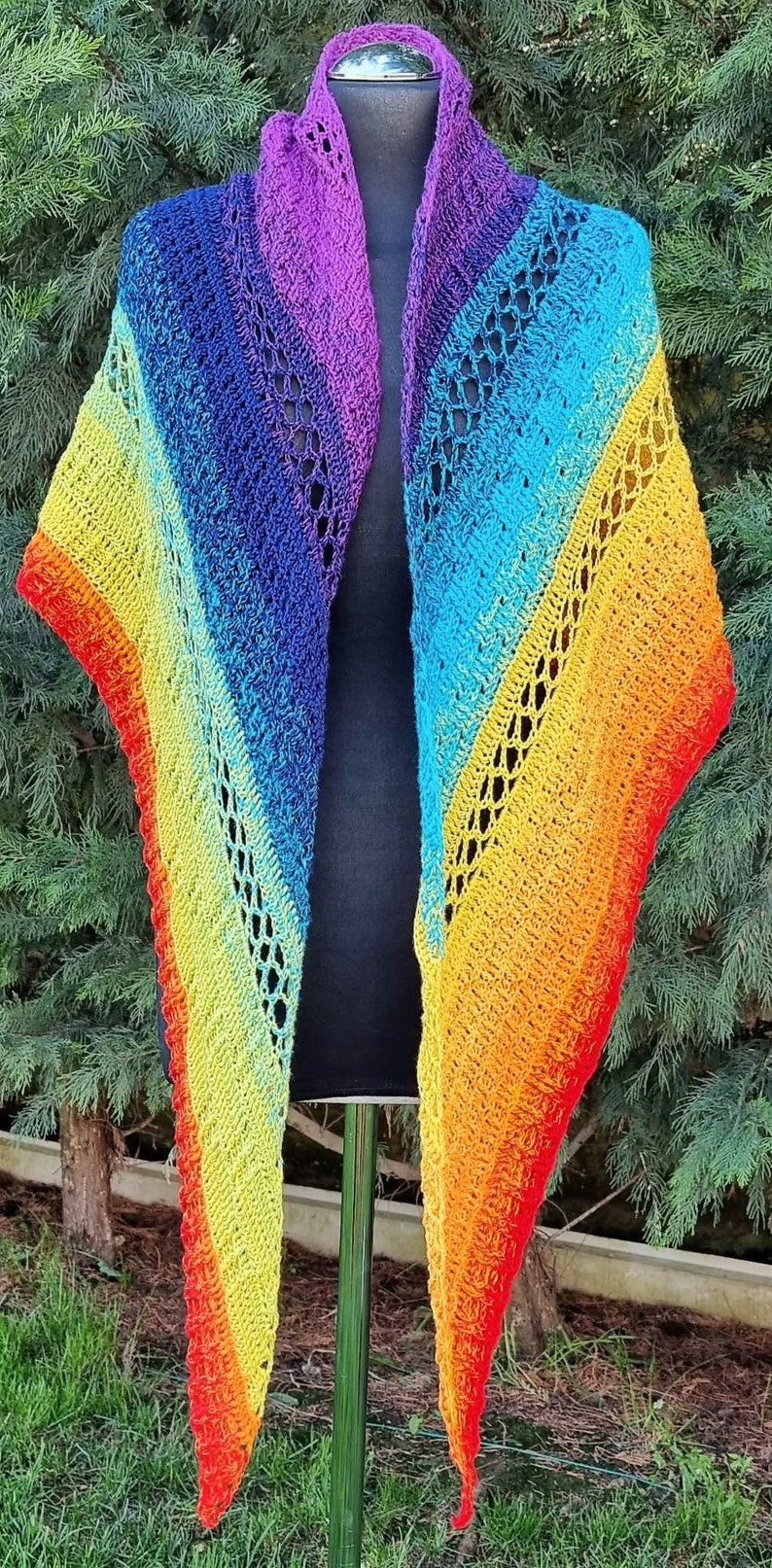 Puede incluir: Un chal de ganchillo de arco&iacute;ris con un patr&oacute;n de encaje. El chal se muestra en un maniqu&iacute; y tiene un degradado de colores de morado a rojo.