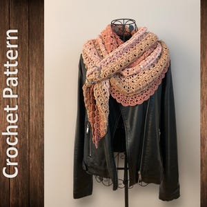 Könnte beinhalten: Ein gehäkeltes Tuch in Rosatönen, Pfirsich und Braun, das über eine schwarze Lederjacke gelegt wird. Das Tuch hat ein zartes Spitzenmuster und einen gewellten Rand.