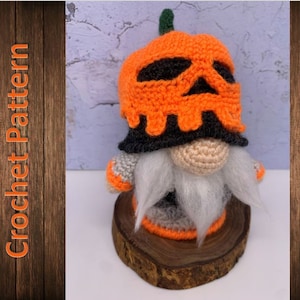 Könnte beinhalten: Ein gehäkelter Zwerg mit einem Kürbis-Hut mit Totenkopf-Design. Der Zwerg sitzt auf einem Holzsockel.