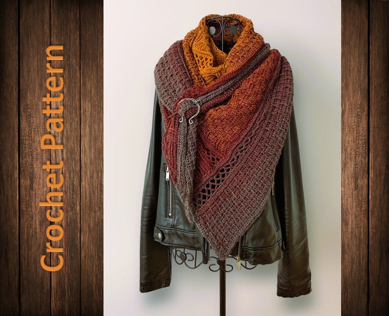 Puede incluir: Un chal de ganchillo triangular en tonos marrones, naranjas y rojos con un anillo de metal decorativo. El chal est&aacute; drapeado sobre una chaqueta de cuero negra.