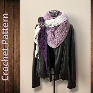 Op de afbeelding: Een zwarte leren jas wordt getoond op een metalen hanger, versierd met een gehaakte sjaal. De sjaal heeft een verloop van wit, lavendel en paars, vastgemaakt met een decoratieve sluiting. De woorden "Crochet Pattern" zijn zichtbaar.