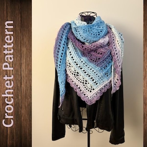 Op de afbeelding: Een handgemaakte gehaakte sjaal in tinten blauw, paars en wit, gedrapeerd over een zwarte jas. De sjaal heeft een open ontwerp en een geschulpte rand. De woorden "Crochet Pattern" staan verticaal aan de linkerkant van de afbeelding.