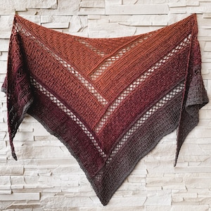 Puede incluir: Una estola de ganchillo triangular con un degradado de tonos naranja, rojo y morado. La estola tiene un patr&oacute;n de encaje y est&aacute; hecha con un hilo suave.