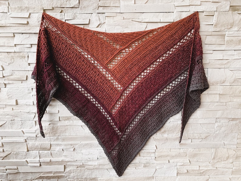 Puede incluir: Una estola de ganchillo triangular con un degradado de tonos naranja, rojo y morado. La estola tiene un patr&oacute;n de encaje y est&aacute; hecha con un hilo suave.
