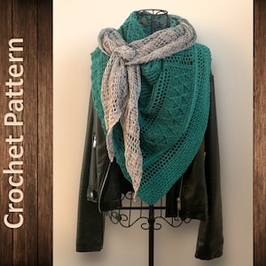 May include: A teal and gray crochet shawl draped over a black leather jacket on a mannequin. The shawl is crocheted in a delicate pattern with a fringe on the edges.