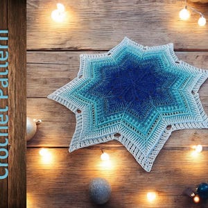 Könnte beinhalten: Gehäkelte sternförmige Tischdecke in Blau- und Weißtönen mit Farbverlauf. Der Text "Crochet Pattern" ist sichtbar. Auf einer Holzoberfläche mit Lichterketten und Dekorationen. Durchmesser ca. 30 cm.