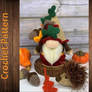 May include: Crocheted gnome with a brown hat and a green and brown leaf design. The gnome is wearing a red and white outfit and has a white beard. The gnome is sitting on a wooden log with a crocheted hedgehog and acorns nearby.
