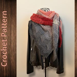 Può includere: Uno scialle all'uncinetto nei toni del rosso, rosa e grigio, drappeggiato su una giacca di pelle nera. Lo scialle presenta un motivo traforato ed è fissato con una spilla dorata a forma di nodo celtico. Le parole "Crochet Pattern" sono visibili.