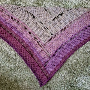 Puede incluir: Un chal triangular de punto de color morado y gris con un patr&oacute;n de encaje.