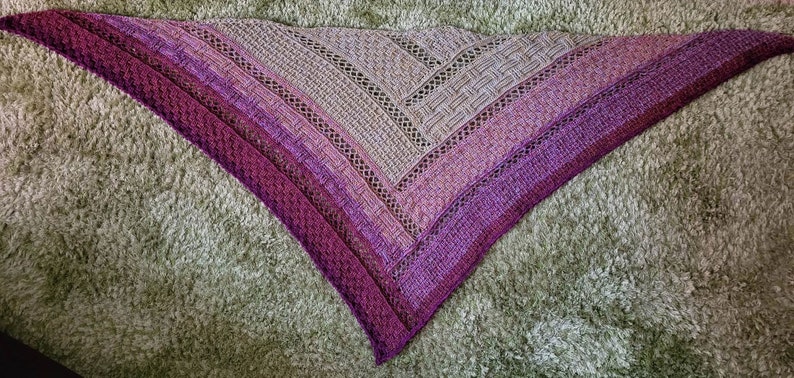 Puede incluir: Un chal triangular de punto de color morado y gris con un patr&oacute;n de encaje.