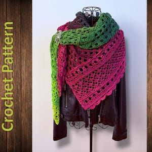 Puede incluir: Un chal de ganchillo hecho a mano en un degradado de colores, de verde a rosa, drapeado sobre una chaqueta de cuero negra. El chal presenta un diseño calado y está asegurado con una broche plateada. Las palabras "Crochet Pattern" son visibles.