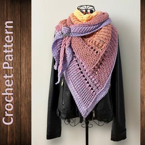 Könnte beinhalten: Ein gehäkeltes Tuch mit einem Farbverlauf von Gelb, Orange, Rosa und Lila. Das Tuch ist über eine schwarze Lederjacke gelegt.