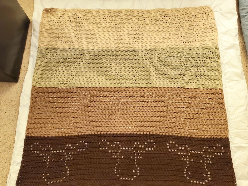 May include: A crocheted blanket with a multi-colored striped pattern. The blanket is made of brown, beige, and green yarn. The blanket has a lacy design with open spaces.