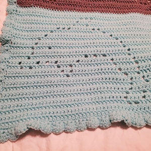 May include: A handmade crochet blanket in shades of teal and brown. The blanket features a textured stitch pattern with star-shaped cutouts and a scalloped edge. The soft, cozy blanket is perfect for snuggling up.