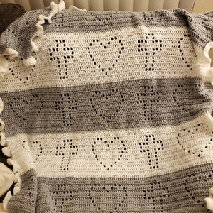 May include: A crocheted baby blanket with a white and grey striped pattern. The blanket has a scalloped edge and features a heart design.