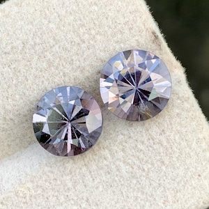 Puede incluir: Dos piedras preciosas redondas y facetadas de color púrpura sobre un fondo blanco.
