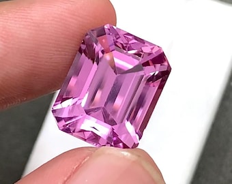 May include: A vibrant pink gemstone with an emerald cut, featuring a rectangular shape and multiple facets that reflect light. The stone displays a clear, saturated pink hue throughout its structure, showcasing precise geometric edges and polished surfaces.