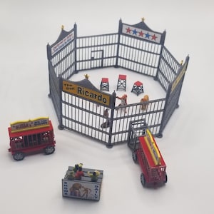 Peut inclure: Un ensemble de cirque miniature avec une cage en métal gris, des chariots de cirque rouges et jaunes et une pancarte indiquant "The Great Ricardo".
