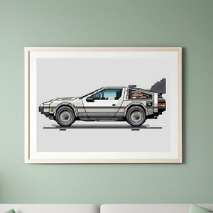 Könnte beinhalten: Ein gerahmter Druck eines weißen DeLorean-Zeitmaschinenautos vor grauem Hintergrund. Das Auto hat silberne Verzierungen und einen schwarzen Innenraum. Das Auto ist nach rechts gerichtet.