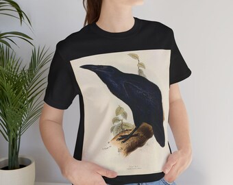 Pode incluir: Camiseta preta com uma ilustração vintage de um corvo empoleirado em um galho. A obra de arte apresenta um corvo preto, folhas verdes e madeira marrom. A camiseta é feita de um material macio.