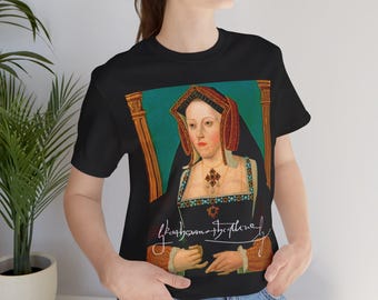 Pode incluir: T-shirt preto com um retrato histórico de uma mulher com um toucado vermelho e dourado e um colar de joias. O texto "Katherine the Queen" está incluído em escrita cursiva.
