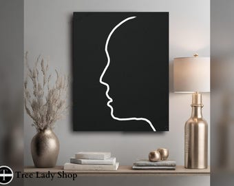 May include: A rectangular wall art piece featuring a stark white continuous line drawing of a human profile silhouette centered on a solid black background. The artwork is displayed in a room setting with a metallic vase and a table lamp nearby.