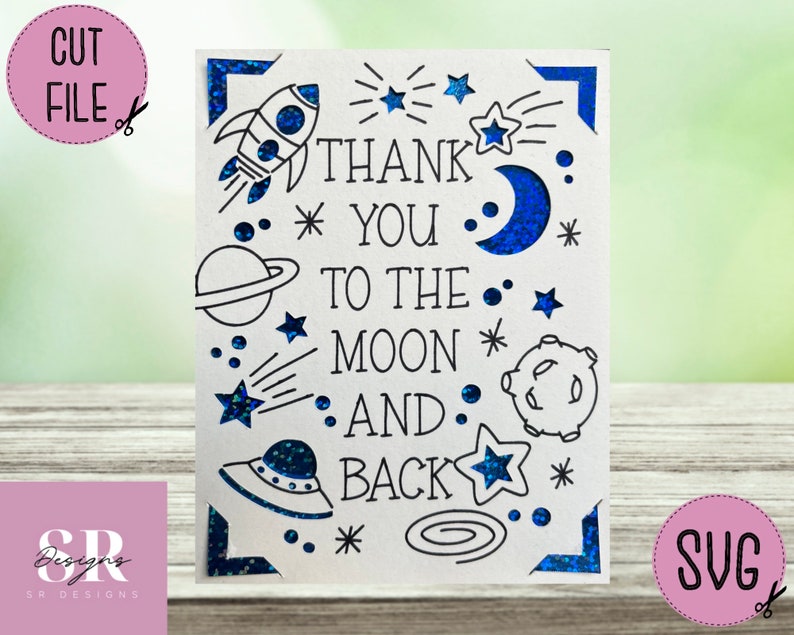 Op de afbeelding: Een witte kaart met een blauwe glitterrand en een ruimtethema. De kaart zegt "Bedankt tot de maan en terug" met sterren, planeten, een raket en een UFO.