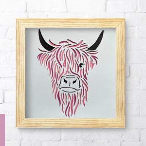 Puede incluir: Un archivo de corte digital de una cabeza de vaca Highland con colores rosa y negro. La cabeza de la vaca est&aacute; enmarcada en un marco de madera claro.