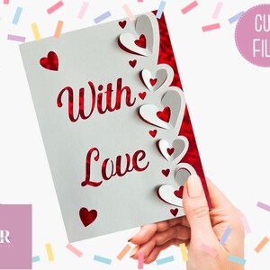 Pu&ograve; includere: Un biglietto bianco con le parole "With Love" in scrittura rossa. Il biglietto ha un bordo decorativo di cuori rossi e bianchi.