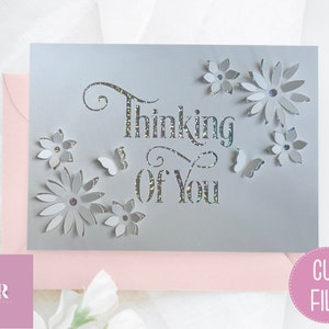 May include: A gray card with the words "Thinking of You" cut out in a decorative font. The card is decorated with white paper flowers and butterflies.