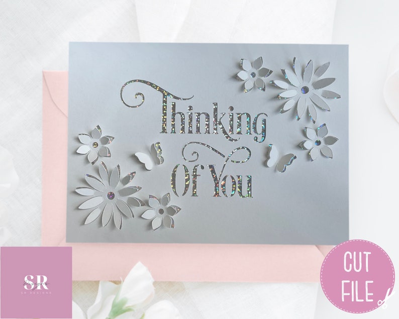 May include: A gray card with the words "Thinking of You" cut out in a decorative font. The card is decorated with white paper flowers and butterflies.