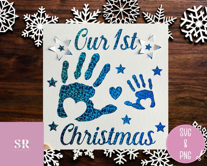 May include: A white card with blue glitter handprints and the text "Our 1st Christmas". The card is surrounded by white snowflake cutouts.