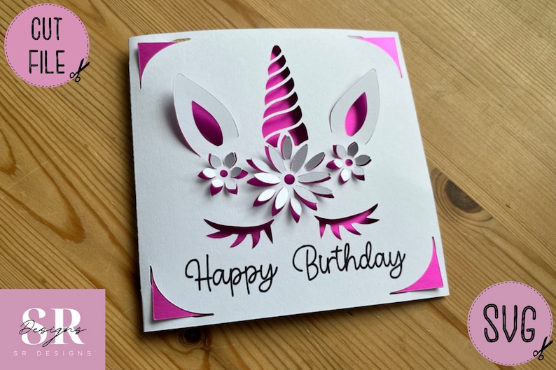 May include: A white card with a pink unicorn design and the text "Happy Birthday". The unicorn has a pink horn, pink ears, and pink eyelashes. There are white flowers around the unicorn's horn.