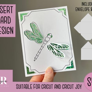 May include: A white card with a green dragonfly design inside a black frame. The card is suitable for Cricut and Cricut Joy. The image also includes a white envelope and liner.
