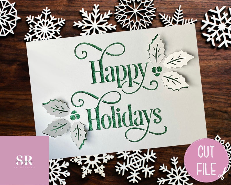 Puede incluir: Una tarjeta blanca con letras verdes brillantes que dicen "Felices Fiestas" con hojas de acebo y bayas a cada lado. La tarjeta est&aacute; rodeada de copos de nieve blancos sobre un fondo de madera.