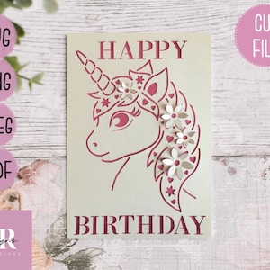 May include: A white card with a pink unicorn silhouette and the text "HAPPY BIRTHDAY". The unicorn has a floral crown and pink accents.