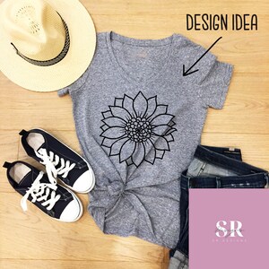 May include: Gray V-neck t-shirt with a black outline of a sunflower design. The shirt is shown on a wooden surface with a straw hat, jeans, and sneakers.